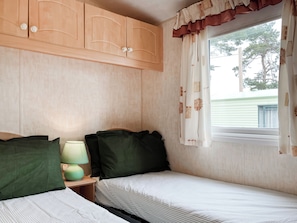 Un dormitorio con dos camas, armarios de madera, una mesita de noche y una ventana con cortinas.