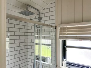 A shower with a glass door, a window with blinds, and a tiled wall.