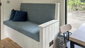 A room with a bench with patterned upholstery, a utility bin, and a view of the outdoors. - Shepherds Hut - UK52010 (Harrogate)