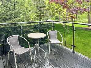 A wooden deck with two wicker chairs and a small round table, surrounded by a glass railing.