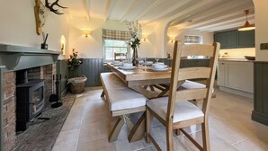 Un comedor con una larga mesa de madera, bancos, una chimenea y una cocina al fondo.