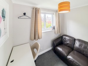 Ein Zimmer mit einer braunen Ledersofa, einem weißen Schreibtisch, einer Pendelleuchte und einem Fenster mit Vorhängen.