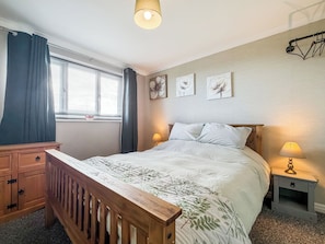 Ein Schlafzimmer mit einem hölzernen Bett, zwei Nachttischlampen, einem Nachttisch, einer hölzernen Kommode und einem Fenster mit Vorhängen.