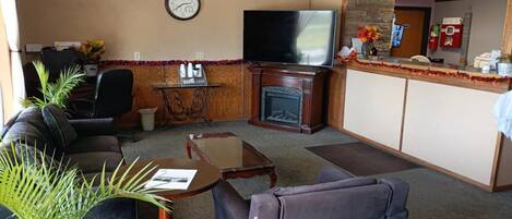 Una sala de estar con sofá, sillón, mesa de centro, chimenea, televisión y mostrador de recepción.