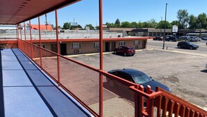 Un parking avec un bâtiment en arrière-plan, une zone bleue abritée avec une rambarde, et plusieurs voitures garées.