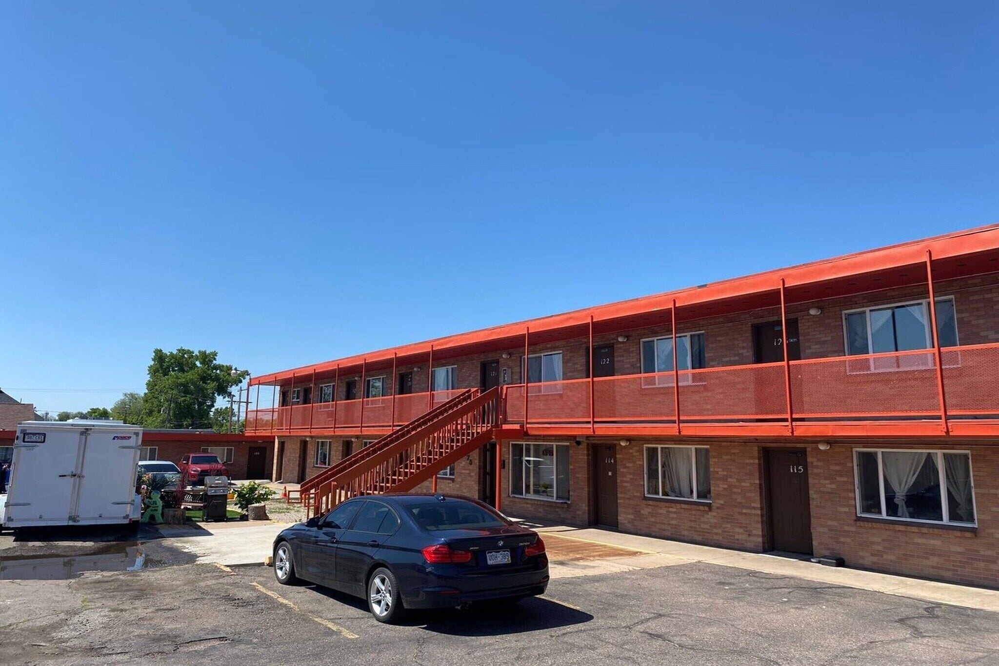 A multi-story building with a red exterior, a staircase, and a parking lot with a car and a trailer.