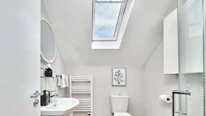 Um banheiro moderno com claraboia, acessórios brancos, vaso sanitário e box de vidro.