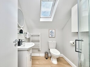 A modern bathroom with a skylight, white fixtures, a toilet, and a glass shower enclosure. - No.3 Princess Blue Apartments (Portrush)