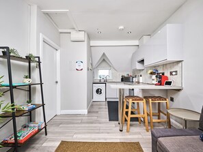 A modern kitchen with a built-in washing machine, wooden stools, and a small dining table. - No.3 Princess Blue Apartments (Portrush)