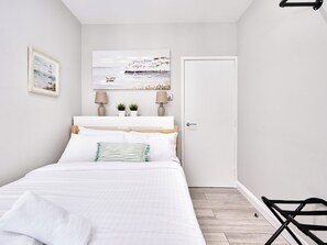 A bedroom with a bed, a door, a chair, a painting, and two lamps. - No.3 Princess Blue Apartments (Portrush)