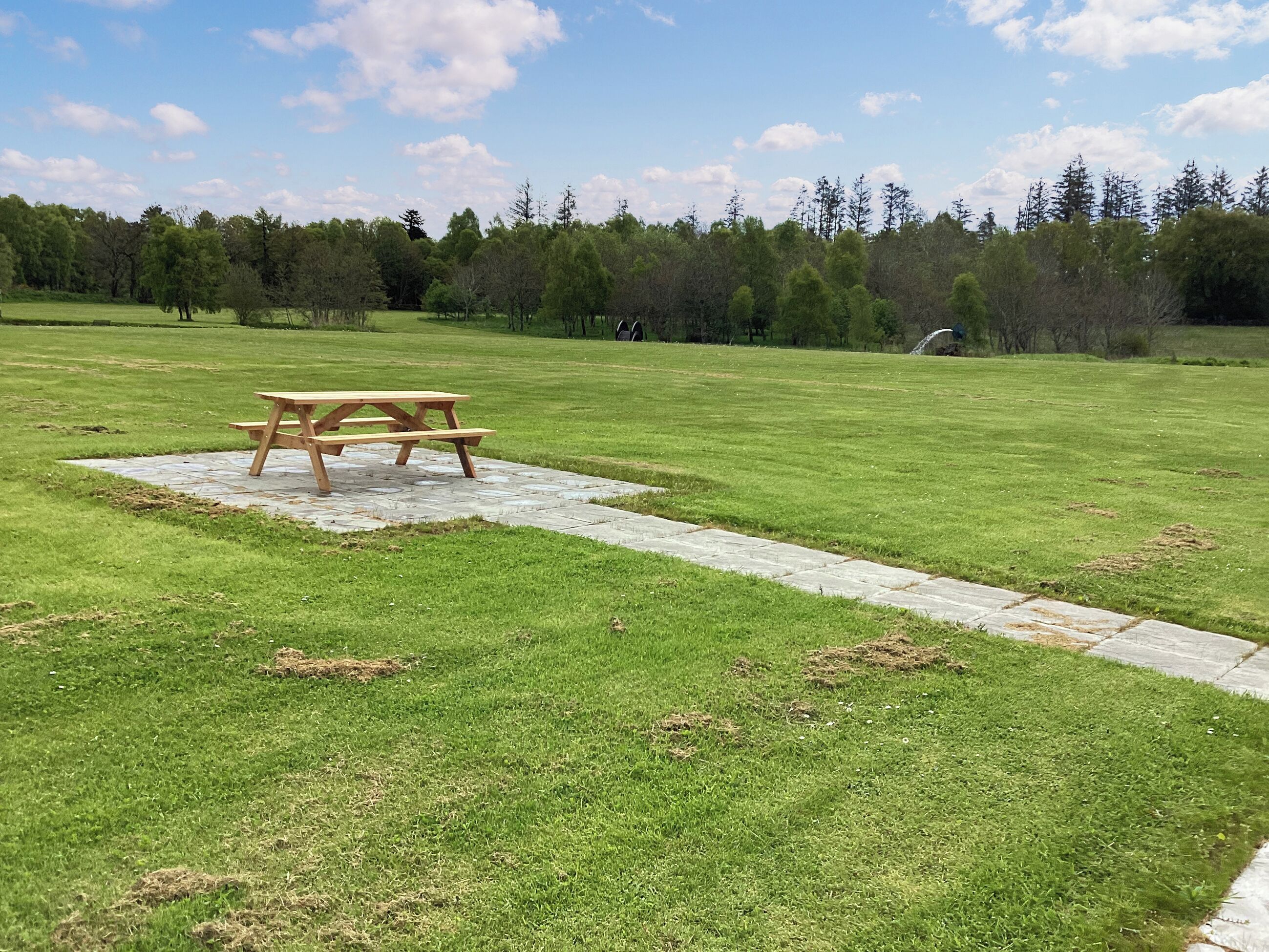 Una mesa de picnic en un campo con césped, con un sendero de piedra que la lleva a ella.