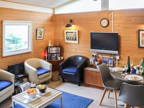 A cozy living room with a TV, seating, a bookshelf, and a dining area with a table set for two.
