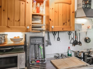A kitchen with wooden cabinets, a microwave, a toaster, and various utensils hanging on the wall. - 3 bedroom accommodation in Cenarth (Cenarth)