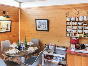 Habitació amb panells de fusta, una taula de dinar preparada per a dues persones, una cafetera i una estantàcia amb utensilis de cuina.