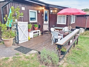Eine Holzterrasse mit Tisch, Stühlen, Topfpflanzen und einer Bank.