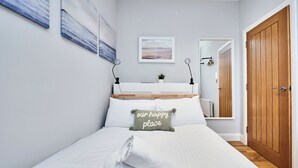 Cama bem arrumada com travesseiro, luminária de cabeceira, uma pequena planta e porta de madeira.