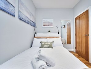 Ein ordentlich bezogenes Bett mit Kissen, einer Nachttischlampe, einer kleinen Pflanze und einer Holztür.