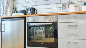 Uma cozinha compacta com geladeira, forno e armários brancos.