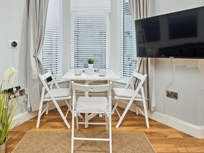 Ein Zimmer mit einem weißen Tisch, zwei Stühlen, einem Fernseher und einem Fenster mit Jalousien.