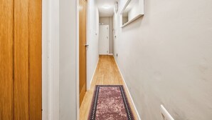 Un pasillo estrecho con puertas de madera, un tapete estampado y una lámpara en el techo.