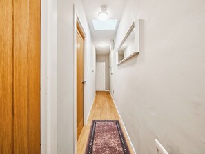 A narrow hallway with wooden doors, a patterned rug, and a ceiling light fixture. - No.5 Princess Green Apartments - UK52039 (Portrush)
