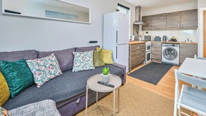 Un espacio habitable compacto con un sofá, una mesita redonda, lavadora y kitchenette.