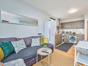 Ein kompakter Wohnbereich mit Sofa, rundem Tisch, Waschmaschine und Küchenzeile.