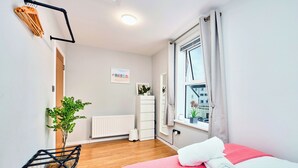 Un dormitorio con cama, un radiador, una ventana con cortinas, una planta y un aparador blanco.