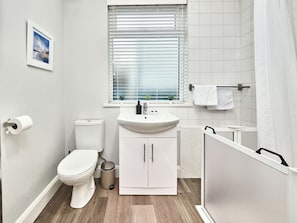 A compact bathroom with a toilet, sink, and window with blinds. - No.1 Princess Yellow Apartments - UK52052 (Portrush)