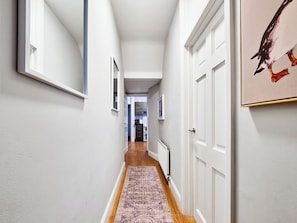 A hallway with white walls, wooden flooring, and a patterned rug. There are white doors on the right and a framed picture on the left. - No.1 Princess Yellow Apartments - UK52052 (Portrush)