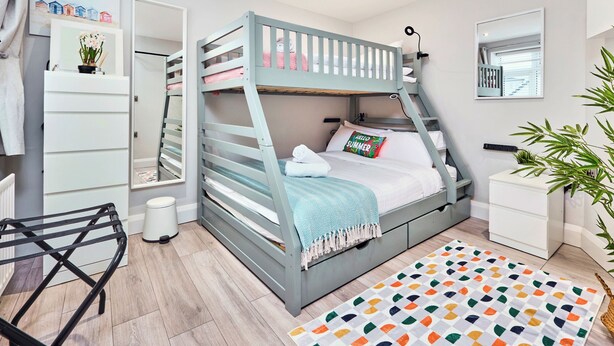 Un lit superposé avec une tête de lit, une table de chevet, un miroir, une petite plante et un tapis coloré.
