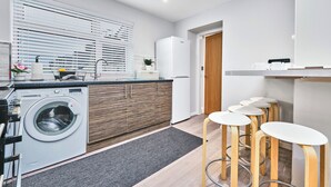 Une cuisine moderne dotée d’un lave-linge encastré, de meubles en bois et d’un coin bar avec des tabourets.