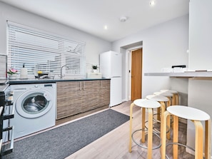 Een moderne keuken met een ingebouwde wasmachine, houten kastjes en een bar met krukken.
