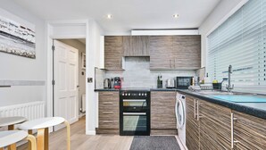 Une cuisine moderne dotée d’appareils électroménagers intégrés, un coin repas avec des tabourets et une vue sur l’extérieur.