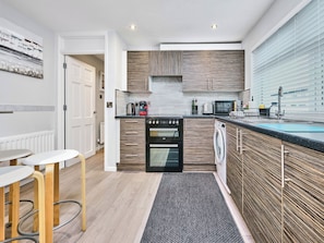 Een moderne keuken met inbouwapparatuur, een eethoek met krukken en uitzicht op buiten.