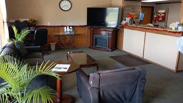 Een woonkamer met een bank, fauteuil, salontafel, open haard, televisie en een receptiebalie.