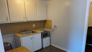 Een kleine keuken met witte kastjes, een houten aanrecht, een spoelbak, een magnetron en een koelkast.