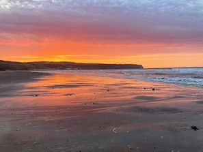 A beach with a sunset, waves, and a distant cliff. - 3 bedroom accommodation in Dunsley, near Sandsend (Dunsley, near Sandsend)
