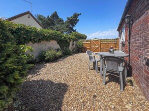 A patio with a table and chairs, a gravel path, a wooden fence, and a brick wall. - 2 bedroom accommodation in Hevingham, near Wroxham (Hevingham, near Wroxham)