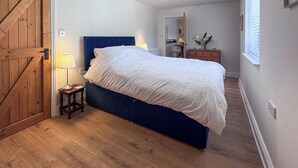 Una camera da letto con un letto, pavimento in legno, una cassettiera, una lampada e una porta.