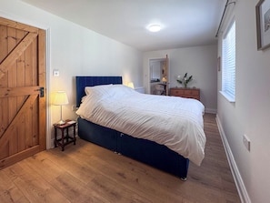 Ein Schlafzimmer mit einem Bett, Holzboden, einem Schminktisch, einer Lampe und einer Tür.