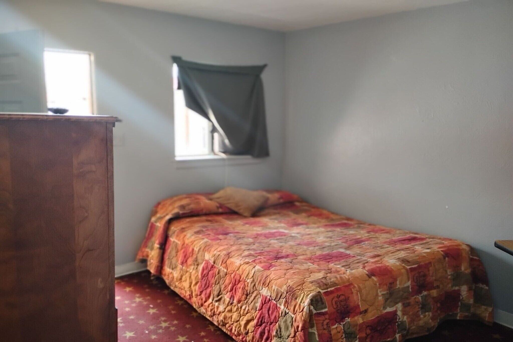 A bedroom with a bed, a window with a curtain, and a wooden dresser.