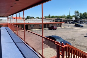 Un estacionamiento con un edificio al fondo, una zona cubierta azul con barandilla, y varios coches aparcados.