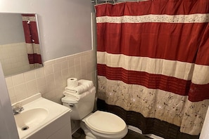 A bathroom with a toilet, sink, and a shower curtain. - Queen Bed | South Denver CO (Englewood CO)