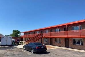 A multi-story building with a red exterior, a staircase, and a parking lot with a car and a trailer.