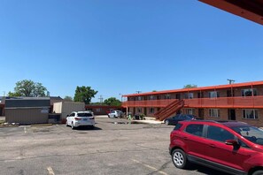 A parking lot with several cars, a red building with a staircase, and a smaller structure to the left.