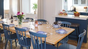 Zona pranzo con tavolo in legno apparecchiato per sei persone, sedie blu e cucina sullo sfondo.
