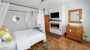Ein Schlafzimmer mit einem Bett, einer Holzkommode, einem an der Wand befestigten Fernseher und einem Spiegel über der Kommode.