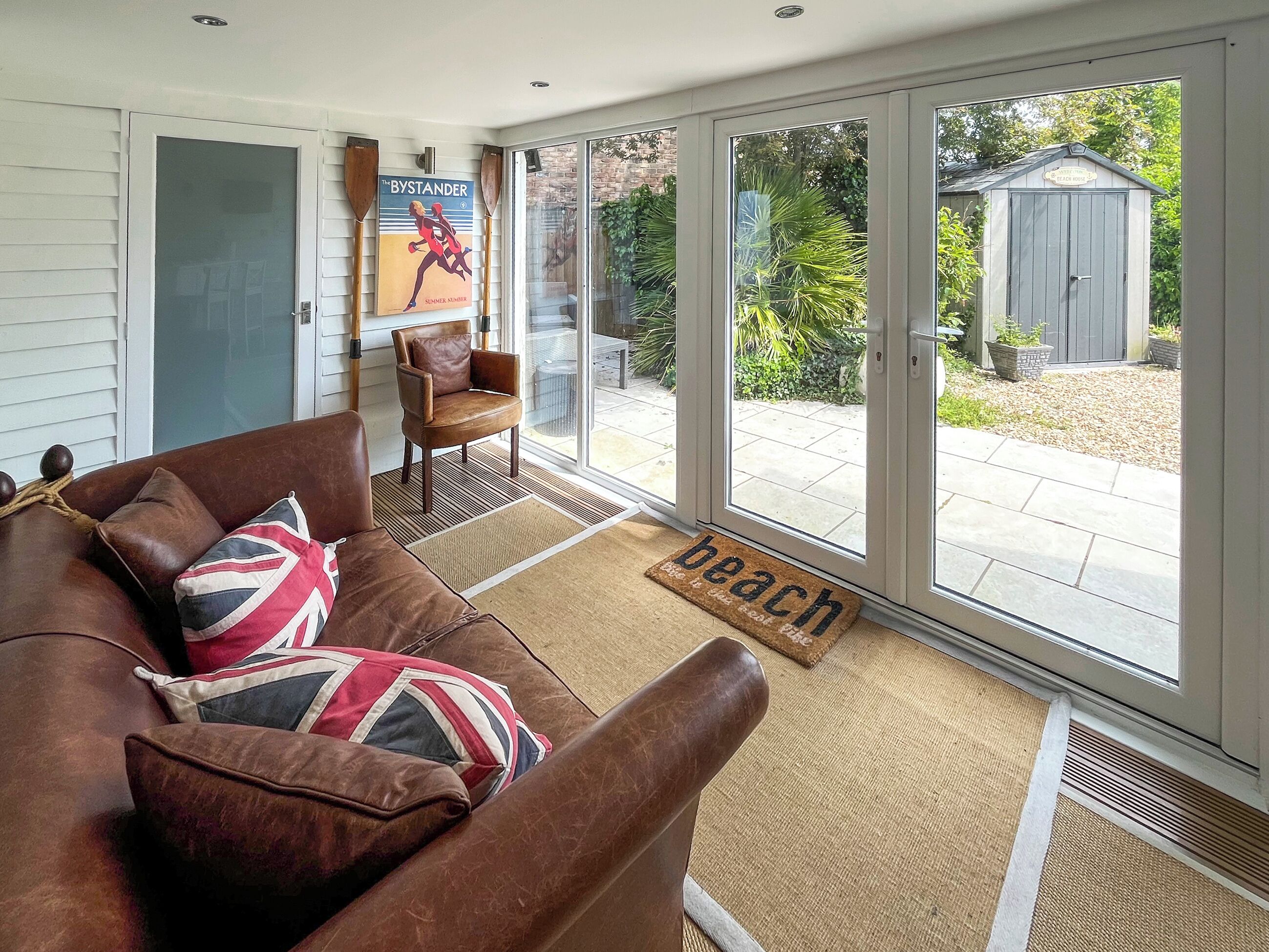A living room with a brown leather couch, a wooden chair, a framed poster, and a glass door leading to a patio.