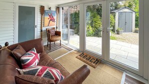 Ein Wohnzimmer mit einem braunen Ledersofa, einem Holzstuhl, einem gerahmten Poster und einer Glastür, die auf eine Terrasse führt.